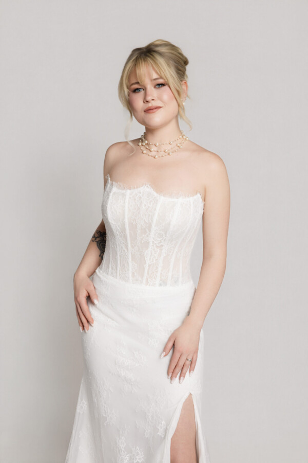 Close-up of a bride wearing a strapless lace corset-style wedding dress with a fitted bodice and subtle floral detailing.