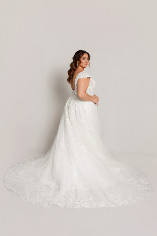 Back and side view of a bride in a lace wedding gown with cap sleeves and a full skirt with a long train.