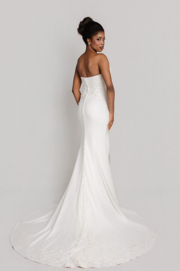Back view of a bride in a strapless fitted wedding gown with a sleek silhouette and long flowing train.