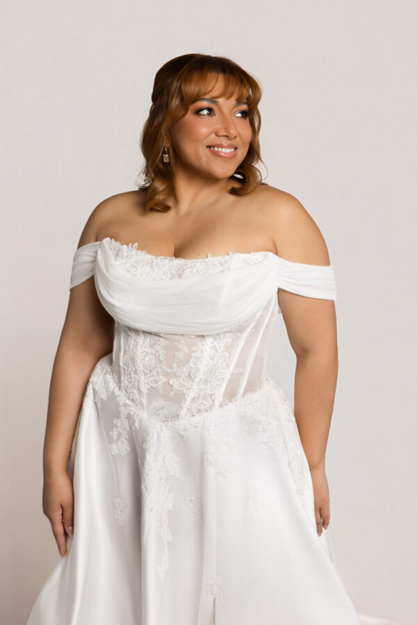 Close-up of a smiling bride wearing an off-the-shoulder white wedding gown with a corset-style bodice.