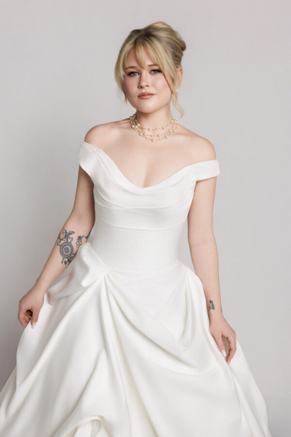 Close-up of a bride wearing an off-the-shoulder white wedding gown with a fitted bodice and draped detailing.