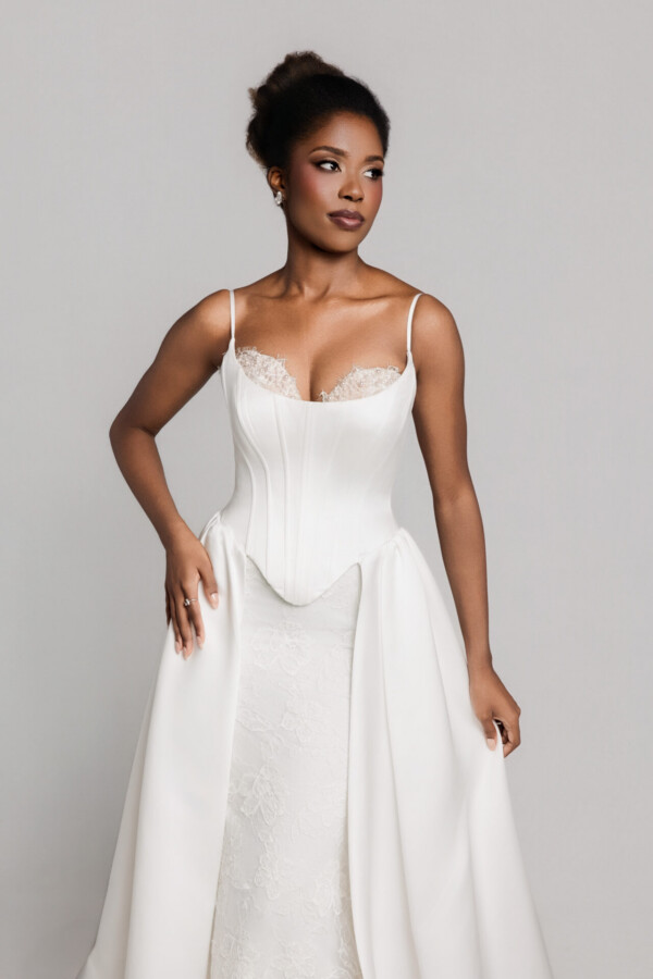Close-up of a bride wearing a white wedding gown with thin straps and a structured bodice, posing against a neutral background.