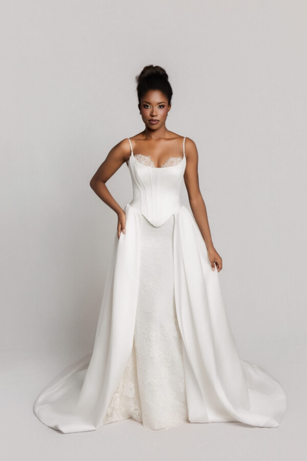 Bride in a strapless white wedding gown with a flowing A-line skirt, standing with one hand on her hip.