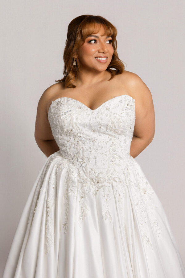 Close-up of a smiling bride wearing a strapless lace wedding gown with a sweetheart neckline and full skirt.