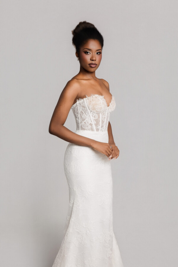 Bride wearing a strapless fitted lace wedding gown with a structured bodice, posing against a neutral background.
