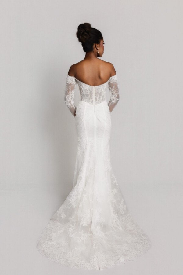 Back view of a bride in an off-the-shoulder lace wedding gown with long sleeves and a fitted silhouette with a lace train.