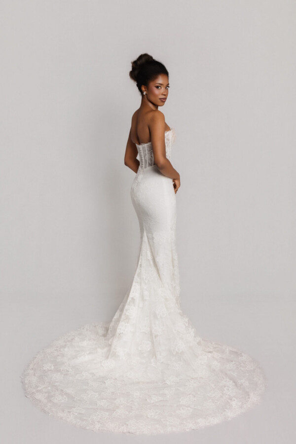 Back and side view of a bride in a fitted lace wedding gown with a long lace train spread behind her.
