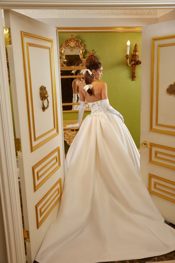 Back view of a bride wearing a satin ball gown with a dramatic full skirt in an elegant room.